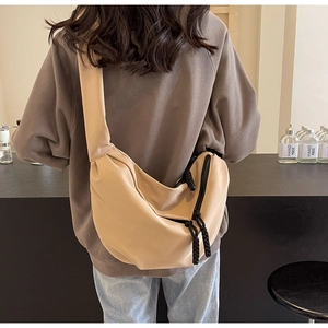 Close-up of a large beige canvas crossbody bag with thick rope zippers on a model's back