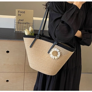 Straw woven tote bag with daisy detail and black straps worn by a model sideways