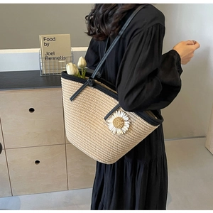 Detail of woven straw shoulder bag with black trim and white daisy flower appliques