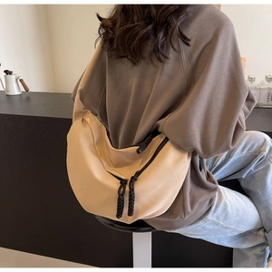 Detail view of a beige crescent canvas crossbody bag with black woven zipper rope