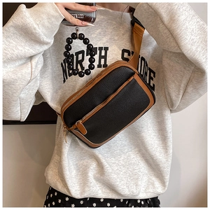 Detail of black pebbled leather crossbody bag with brown trim and woven strap