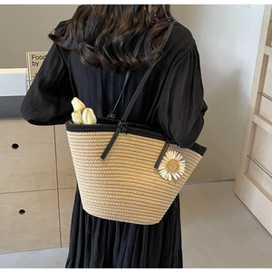 Detail of woven straw tote bag with daisy decoration worn over the shoulder by a model