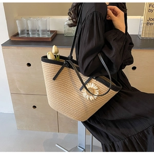 Detail of woven straw tote bag with black leather straps and a decorative daisy flower