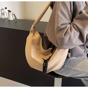 Detail view of a beige crescent crossbody bag featuring a distinctive black woven tassel charm