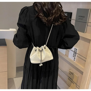 Detail of a creamy white drawstring bucket bag with silver metal chain and pearl pendant