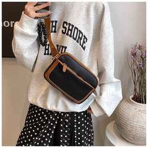 Detail of the black pebbled leather crossbody bag with brown trim and golden zipper