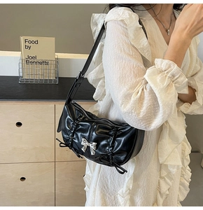 Close-up of black pleated PU bag with silver bow accent on a white dress model
