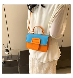 Detail of blue and orange color-block square crossbody bag with large buckle on white shirt