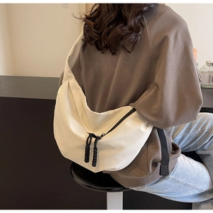 Detail of a cream crescent crossbody bag featuring woven rope zipper pulls on a nylon fabric