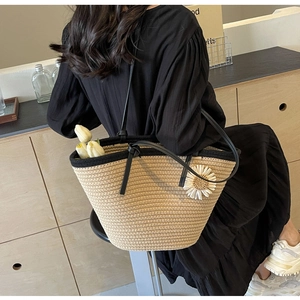 Detail of woven straw tote bag with black leather handles and white daisy floral accent