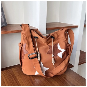 Borsa tote in nylon marrone con toppa a stella e tracolla larga su superficie in legno