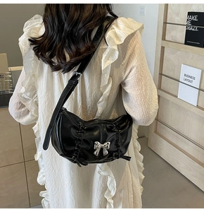 Detail of black ruched half-moon crossbody bag with silver bow buckle and adjustable strap