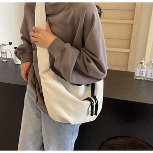 Detail of white slouchy hobo bag featuring contrast black braided zipper pulls and wide strap