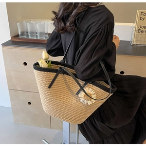 Detail of woven straw tote bag with black handles and a white daisy floral charm accessory