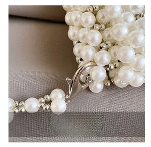 Detailed macro view of an elegant white pearl handbag strap with a silver lobster clasp
