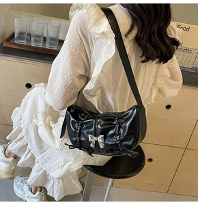Detail of black pleated PU leather shoulder bag featuring a silver metal bow accent