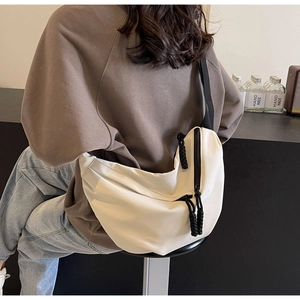 Detail of a beige crescent crossbody bag with black zipper and woven pull on a female model