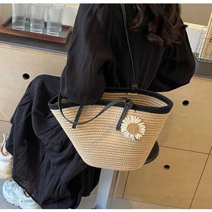 Detail of hand-woven straw tote with black fabric trim and white daisy flower accessory