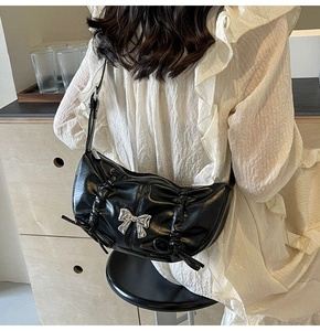 Detail of black ruched PU leather bag with silver metal bow and ribbon accents