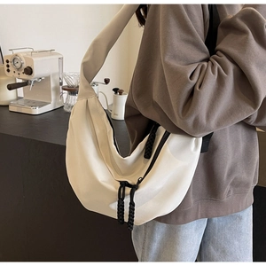 Detail of cream nylon half-moon crossbody bag with woven black zipper pull on a model
