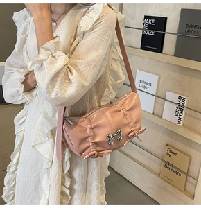 Pink PU leather crossbody bag with silver bow charm worn by a model in a white dress