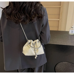 Detail of white velvet drawstring bucket bag with metal chain and pearl charms on model