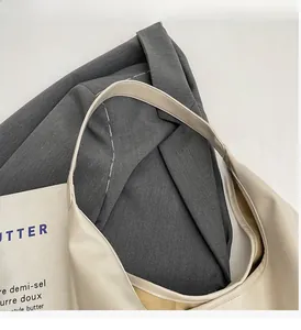Detail view of beige PU leather tote bag with wide strap on grey suit and newspaper