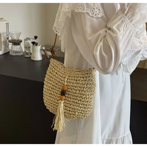 Detail der handgewebten Stroh-Umhängetasche mit Holzperlen und Quaste auf weißem Kleid