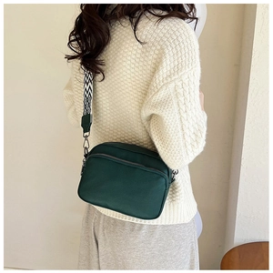 Sac bandoulière vert foncé avec sangle géométrique porté sur un pull en maille blanc
