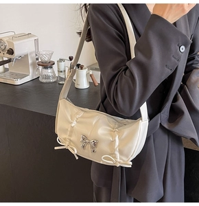 Detailed view of the creamy white pleated shoulder bag with a silver metal bow accent