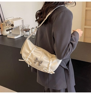 Close-up of cream PU leather handbag featuring silver bow detail and pleated texture