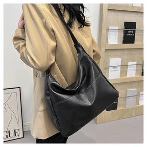 Detailed side view of a black hobo shoulder bag in pebbled PU leather worn by a model