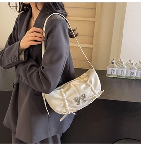 Detail of white pleated PU leather shoulder bag with metal bow and side ribbon accents