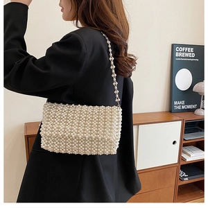 Elegant pearl-woven flap handbag with long shoulder strap worn by a model in a black suit