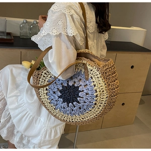 Detail of hand-woven straw tote with blue color-blocking and brown leather strap