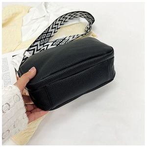 Détail du sac bandoulière noir en cuir grainé avec une large sangle à motifs géométriques