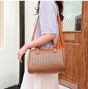 Détail du sac tonneau en paille tissée avec poignées en cuir marron et motif en V
