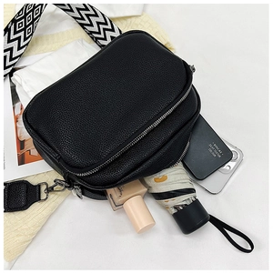 Détail du sac bandoulière en cuir noir à double fermeture et bandoulière rayée