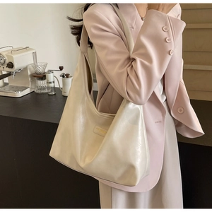 Detail of premium cream PU leather hobo bag with fine texture and metal emblem on side