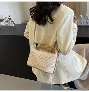 Dettaglio della borsa a tracolla in paglia con finiture in pelle marrone su blazer bianco