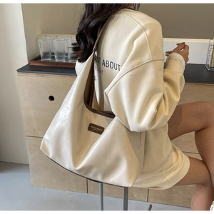 Detail view of cream PU leather tote bag worn by a model in a minimalist setting