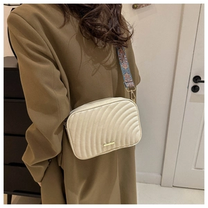 Detail of beige quilted PU bag featuring ethnic woven strap and golden logo plaque