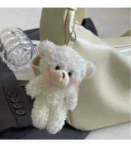 Portachiavi orsetto di peluche bianco con guance rosa su una borsa a tracolla in pelle crema