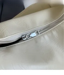 Dettaglio della cerniera in metallo argentato lucido su borsa color crema testurizzata