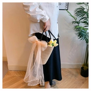 Detailed close-up of woven straw handbag with oversized tulle bow and black handles