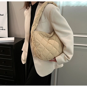 Detail of cream quilted nylon shoulder bag with wavy stitching shown on a model