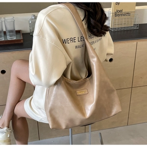 Detail shot of a large brown PU leather tote bag with a golden tag and wide shoulder strap