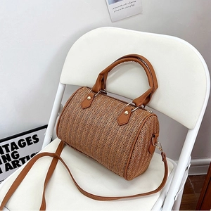 Sac cylindre chic en paille tressée marron avec poignées en similicuir sur chaise blanche