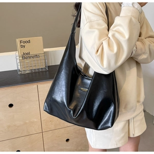 Close-up of black PU leather tote bag with gold metal logo plaque and wide shoulder strap