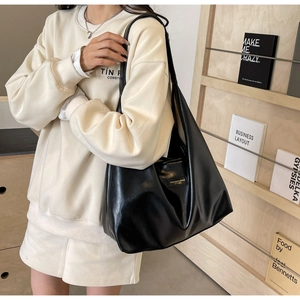 Detail showing matte black leather tote bag with square metal nameplate on a model
